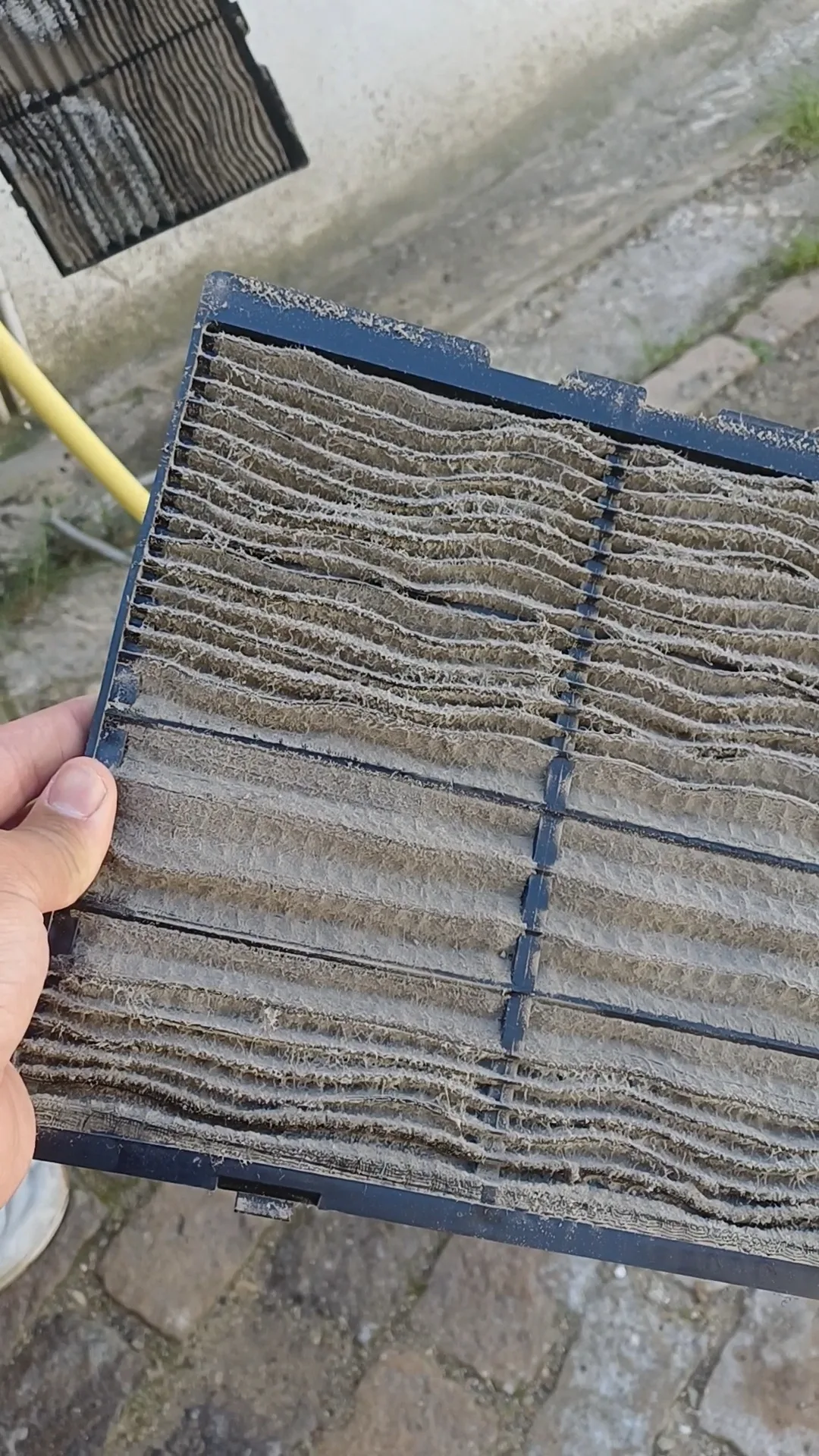 Filtre de climatiseur très encrassé avant nettoyage, tenu à la main